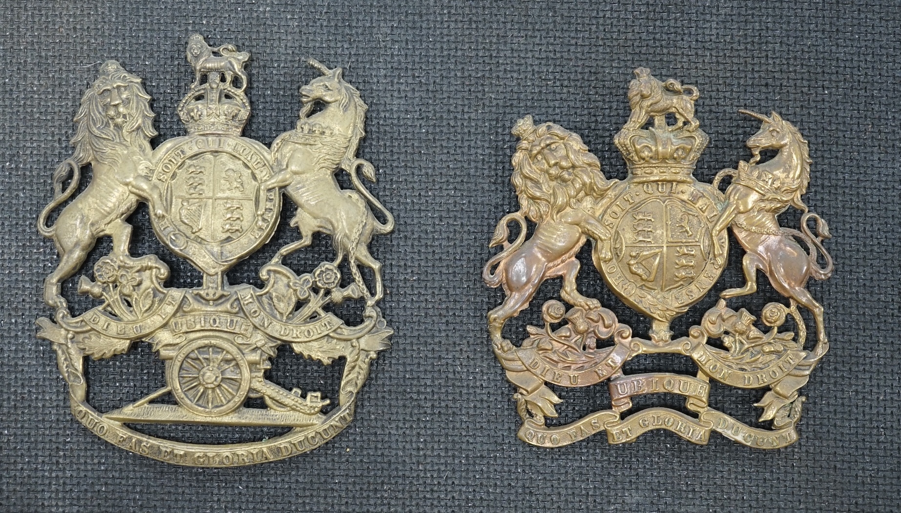 Two Royal Artillery brass helmet plates, one with three lugs and the other with two lugs, loosely mounted onto a backing board. Condition fair to good, top lug missing to one